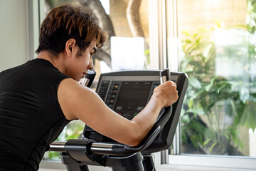 Asian sport man with well trained body in black sportswear cycling on upright stationary bike. Indoor cardio workout in fitness gym © Summer Paradive