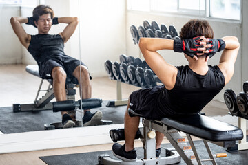 Fototapeta na wymiar Asian Sport man with well trained body in black sportswear lying on workout bench doing sit-up in fitness gym, warming up before weight training. Bodybuilding concept