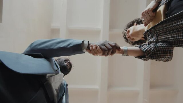 Bottom view camera roll male African American and female Caucasian office workers ending up meeting and shaking hands