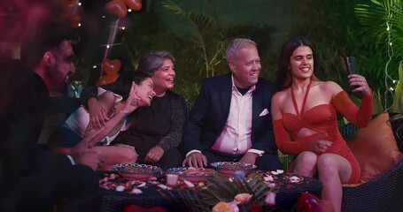 Asian Indian happy young girl sibling using mobile phone take selfie old senior aged man male wife house active teen friends group sitting around table chair enjoy fun joy night dinner party home