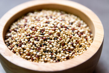 Pile of mixed raw quinoa (Three colors) in wooden bowl on grey background. Quinoa provides protein, dietary fiber, B vitamins, and dietary minerals in rich. Super food of life.