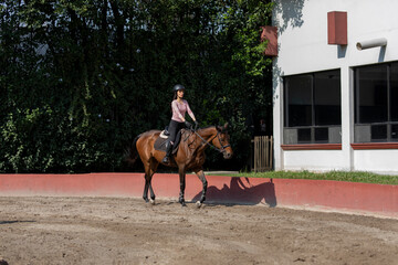 A young woman riding a horse in an equestrian center while practicing