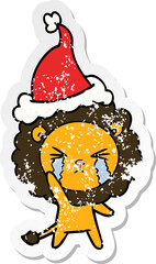 hand drawn distressed sticker cartoon of a crying lion wearing santa hat