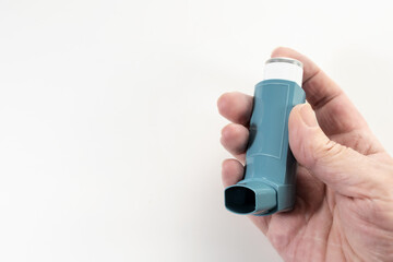 Hand holding a blue inhaler, also known as pump or allergy spray, medical device for asthma or COPD patients, light background, large copy space, selected focus - obrazy, fototapety, plakaty