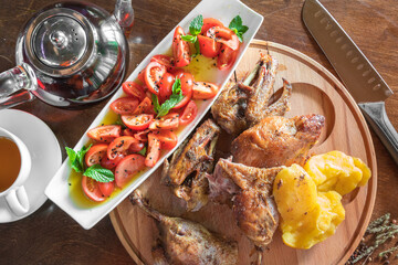 Roasted duck with golden crust, potatoes and red cherry tomatoes with metal kettle on wooden background.