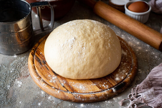 Sweet yeast dough for sweet buns on a wooden board on a gray background. Close-up.