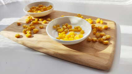 Lot of pieces of canned yellow corn on plate which is on wooden bamboo cutting board on white background. The concept of cooking and delicious healthy food