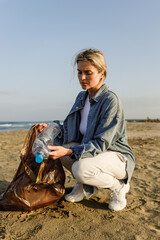 Angry woman volunteer is collecting plastic waste on the beach to contribute to the effort of...