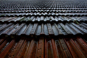 Telhado antigo em perspectiva com telhas molhadas pela chuva em close up.
