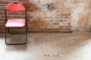 roter Klappstuhl auf Holzfußboden vor unverputzter Ziegelwand - obrazy, fototapety, plakaty