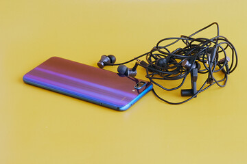 Phone and tangled phone headphone wires side by side on yellow background..