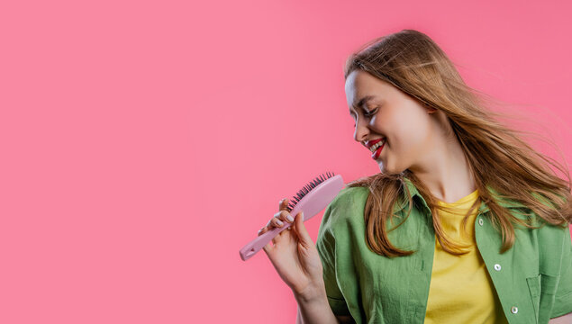 Woman singing, dancing with hair brush instead microphone on pink. Copy space