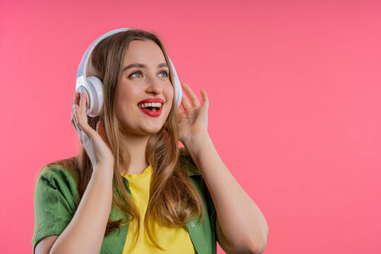 Positive blonde woman listening music, enjoying headphones on pink. Copy space.