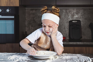 Cooking or Culinary school for children, kids. Little girl with hands and a face smeared in flour,...