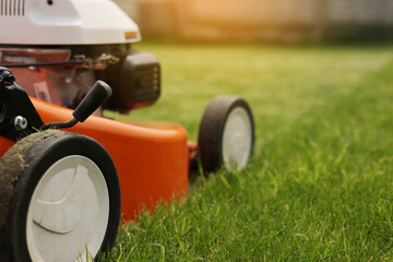 Gardening work tools. Close up details of orange electric lawn mower, wheels, motor on bright lush...