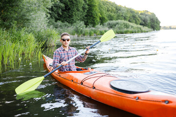 A young Caucasian man sits in a kayak and paddles. The concept of water entertainment.