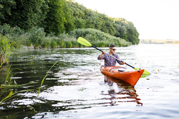 A young Caucasian man sits in a kayak and paddles. The concept of water entertainment.