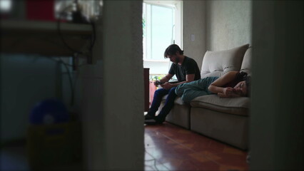 Lonely couple feeling alone at home apartment. Boyfriend looking at smartphone device while woman feels desolate while lying on couch