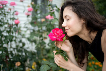 Obraz na płótnie Canvas pretty brunette female smelling bloom roses and enjoying in garden outdoors
