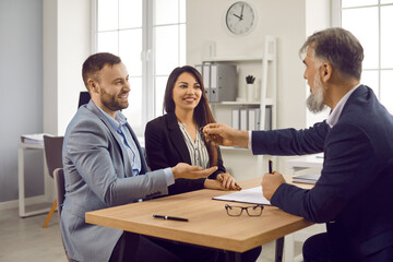 Real estate agent giving keys to couple of customers. Cheerful spouses buying their new home and receiving keys from male realtor. Family buying property, mortgage investment concept