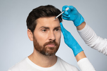 Revitalizing beauty. Middle aged man receiving filler injection into forehead zone, willing to look...