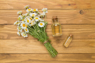 Small bouquet of chamomile flowers with essential oil on wooden background, top view