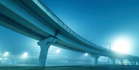 Fototapeta premium Road overpass. Panorama with bridge in evening. Modern overpass bottom view. Road transport infrastructure of city. Road junction under night sky. Overpass on giant columns. Sunset over bridge.