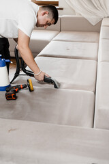 Cleaner is cleaning couch with washing vacuum cleaner extractor machine for dry clean upholstered...