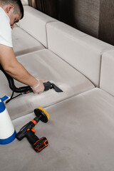 Cleaner is cleaning couch with washing vacuum cleaner extractor machine for dry clean upholstered...