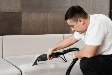 Housekeeper is extracting dirt from upholstered sofa using dry cleaning extraction machine. Cleaner...