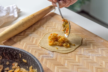 The cook puts the filling on the dough in the home kitchen. Photo