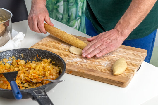 The cook rolls out the dough with a rolling pin in the home kitchen. Dough, stewed cabbage and rolling pin on the table. Photo