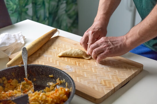 A male cook bakes pies with cabbage in the home kitchen. Dough, stewed cabbage and rolling pin on the table. Photo