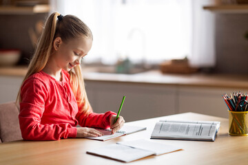 Fototapeta Cute little caucasian girl doing school homework, writing and reading at home obraz