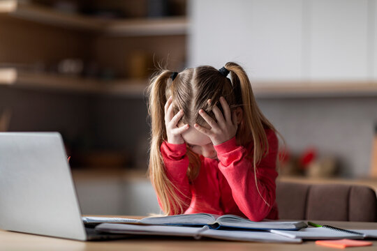 Little schoolgirl suffering while doing homework, tired of reading book