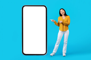 Cheery asian lady pointing at huge phone with white screen