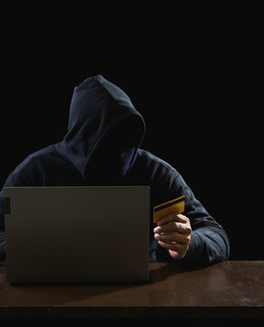 Hacker spy man one person in black hoodie sitting on a table looking computer laptop used login password attack security to circulate data digital in internet network system, night dark background.