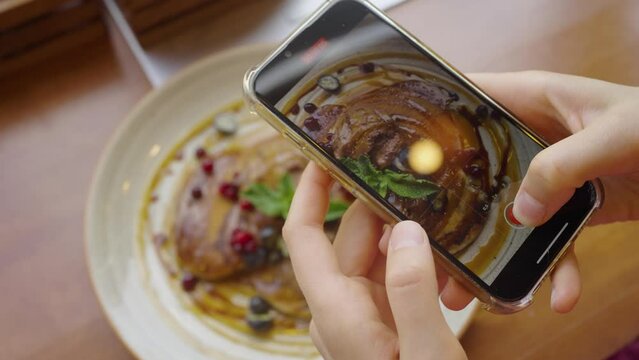 Woman in a cafe takes pictures of vegetarian rice pancakes decorated with mint and berries on a phone camera, close-up hands