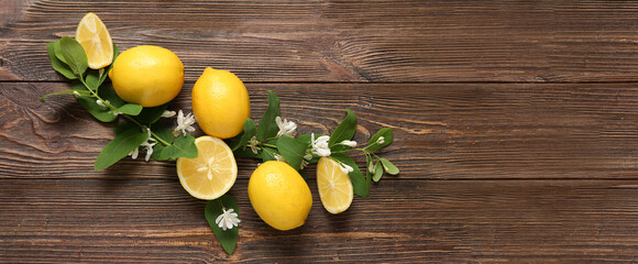 Fresh yellow lemons with green leaves and flowers on wooden background with space for text