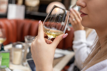 Unrecognizable woman holding clean glass with white wine near face. Adult lady in French restaurant...
