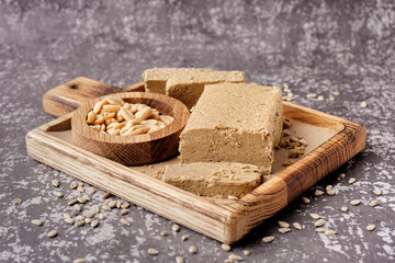 Board with pieces of tasty halva, peanuts and sunflower seeds on grey background