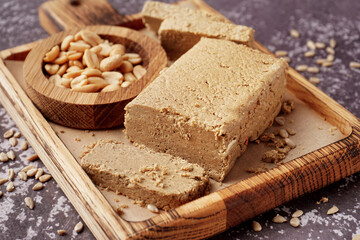 Board with pieces of tasty halva, peanuts and sunflower seeds on grey background