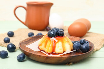 Plate with delicious pudding and blueberries covered by caramel syrup on green wooden table