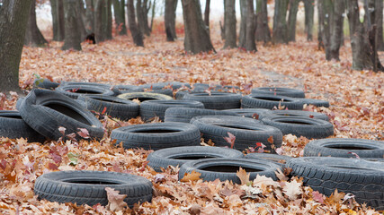 garbage from a heap of black old car tires among the trees in nature. environmental pollution....