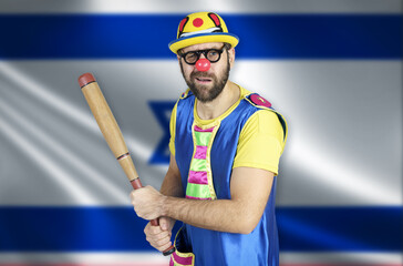 An insecure clown holds a bat in his hands against the background of the flag of Israel