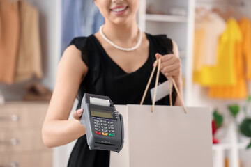 Female sales assistant with payment terminal and shopping bag in boutique, closeup