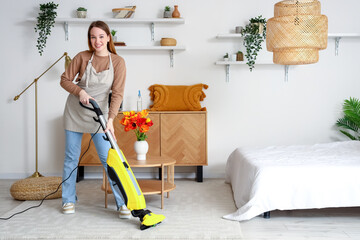 Young woman hoovering carpet in bedroom