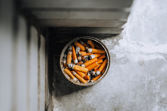 A homemade ashtray from a tin can, an urn with cigarette butts stands in the corner of a brick wall for outdoor garbage. Close-up photo, the concept of the dangers of smoking.