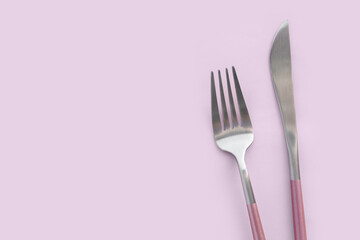 Stainless steel fork and knife on pink background