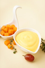 Bowl with tasty cheddar cheese sauce, thyme and grape on beige background, closeup